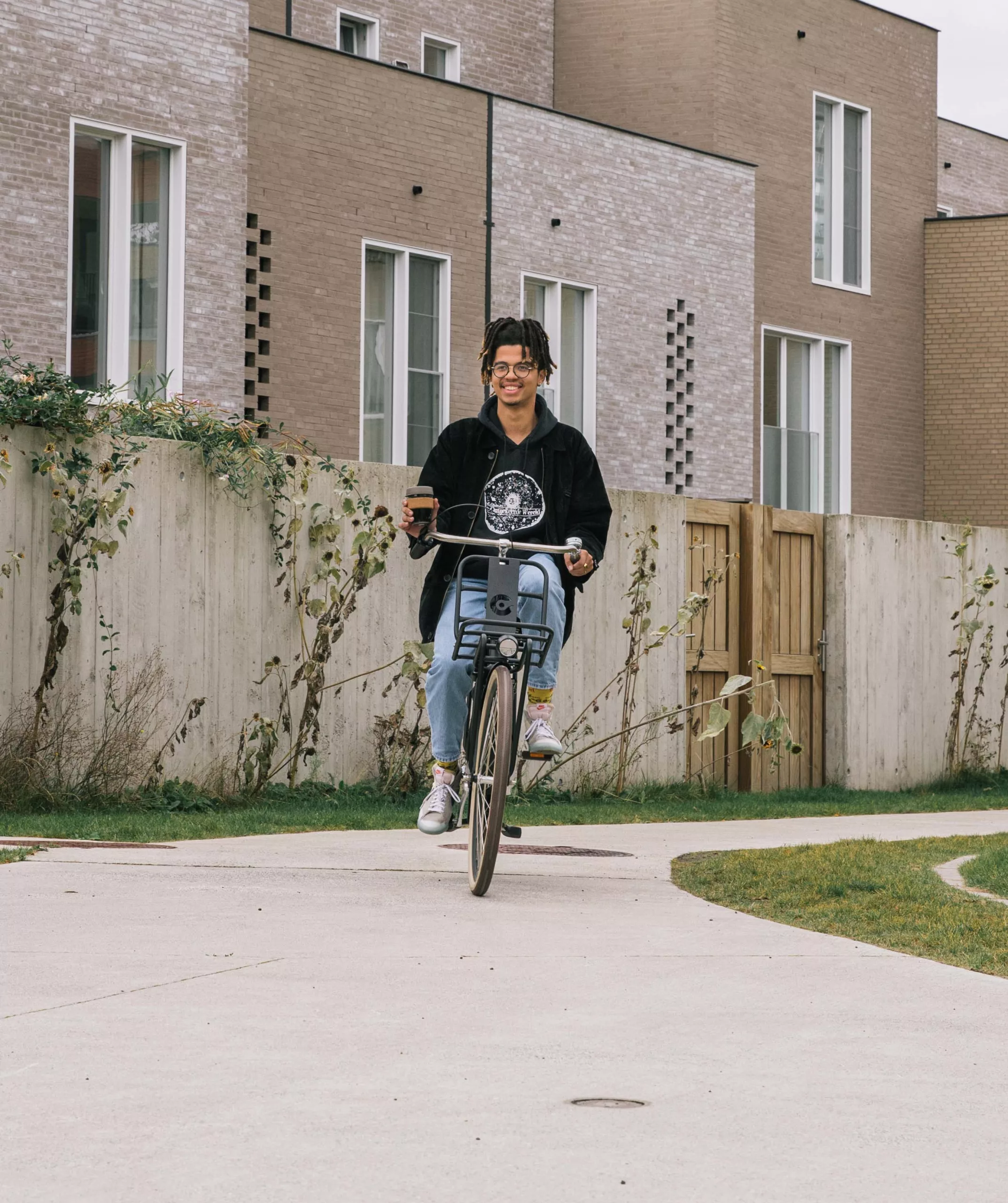 man fietst door een duurzame woonwijk met kop koffie
