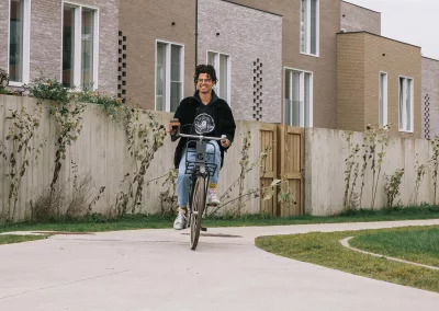 man fietst door een duurzame woonwijk met kop koffie