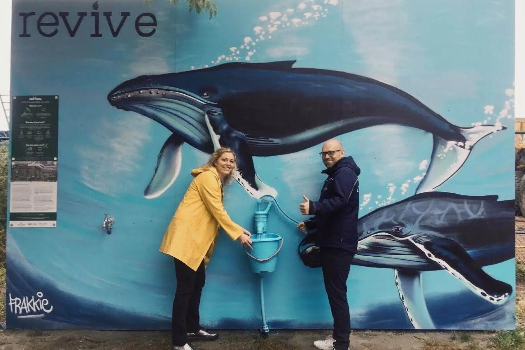 twee mensen nemen water bij een waterpomp met graffiti van walvissen op de muur