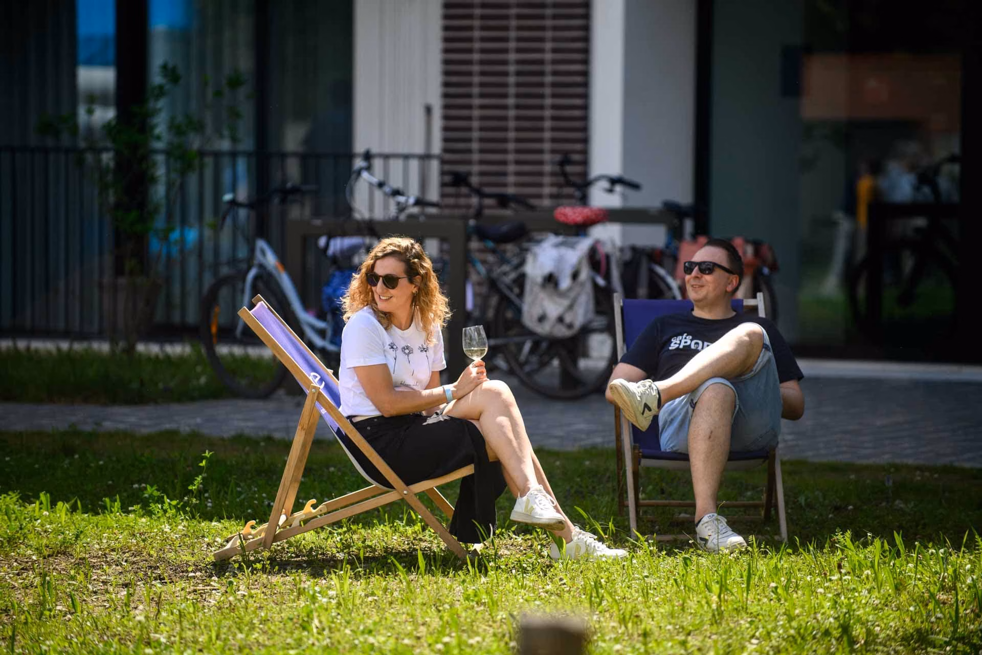 Image of a woman sitting outdoors in park on a grass while listening music with headphones and using mobile phone